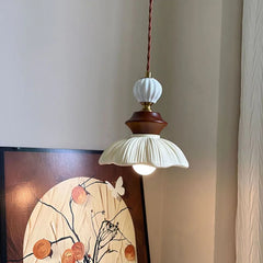 Side view of a cream-style bell-shaped pendant light with a walnut middle section, shown in a room setting next to artwork.