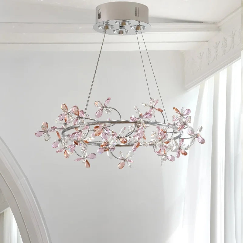 A chrome ring chandelier decorated with clear and pink/rose crystal flowers, hanging from a white ceiling.