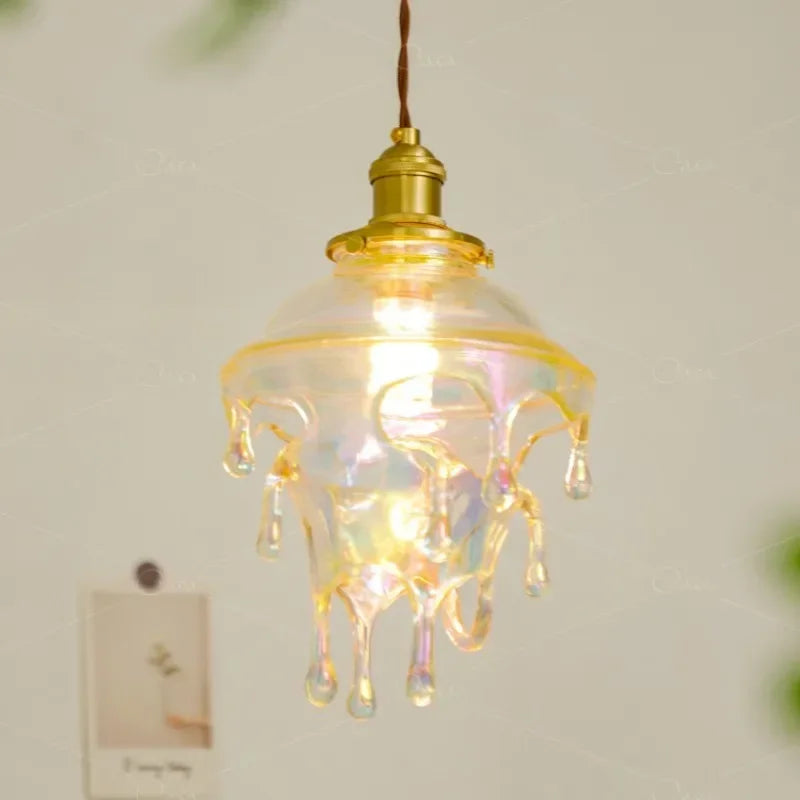 Close-up of a clear glass droplet pendant light with iridescent highlights, lit from within.