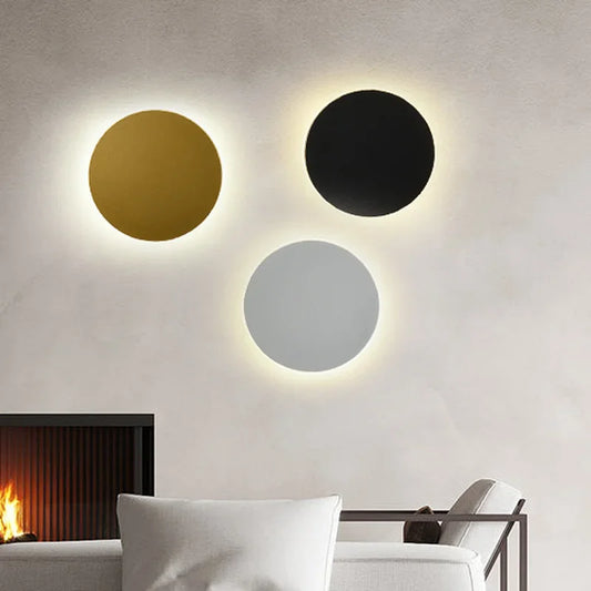 Three circular wall sconces in gold, black, and silver finishes mounted on a wall with soft backlighting.