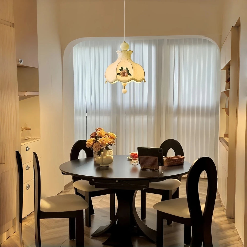 Champagne fabric pendant light with floral rose embroidery hanging over a round dark wood dining table.