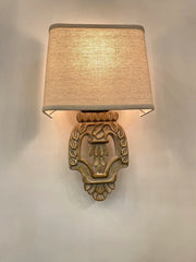 Close-up of a vintage-style wall sconce with a carved wooden base and a light beige fabric shade mounted on a white wall.
