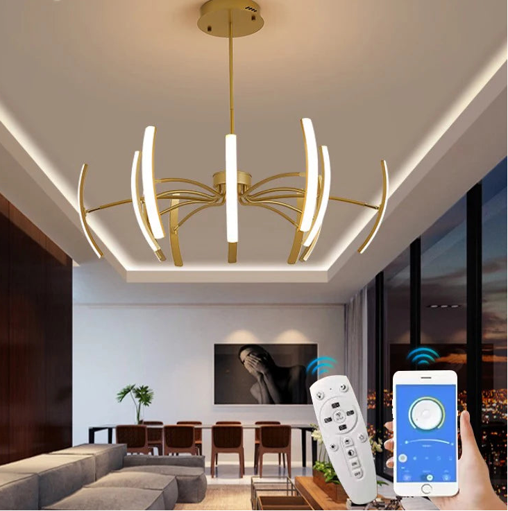 Gold chandelier with curved arms and LED lights in a living room setting, with a remote control and smartphone app visible.
