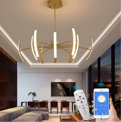 Gold chandelier with curved arms and LED lights in a living room setting, with a remote control and smartphone app visible.