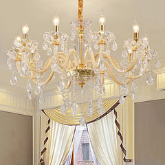 A gold crystal chandelier with multiple arms and dangling crystals, installed in a room with draped curtains.