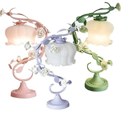 Three table lamps in pink, purple, and green, each with a floral rose vine design and a white frosted bell-shaped shade.