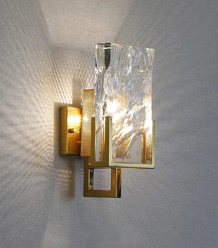 Modern wall sconce with gold and glass design on a textured wall.