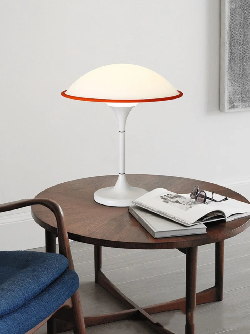 Modern table lamp on a wooden table with a magazine and glasses, in a minimalistic room.