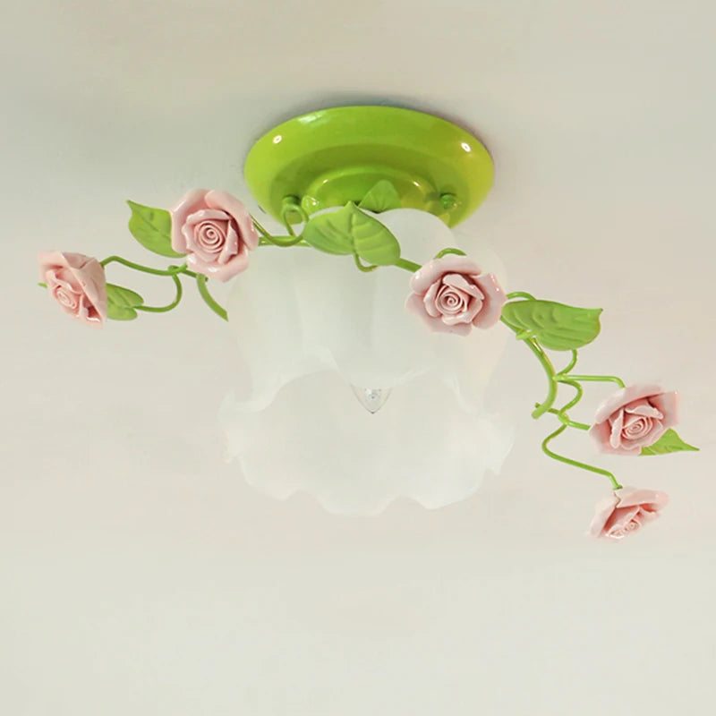 A detailed view of a green base semi-flush ceiling light with pink ceramic roses and green leaves curving around its frosted glass shade.