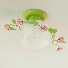 A detailed view of a green base semi-flush ceiling light with pink ceramic roses and green leaves curving around its frosted glass shade.