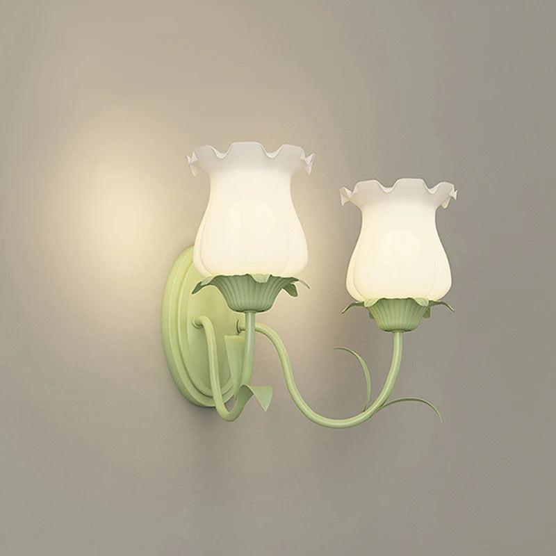 Two green floral wall sconces with frosted glass shades, illuminated on a plain wall.