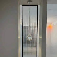 A modern glass globe pendant light hanging in a hallway with vertical ribbed glass paneling in the background.