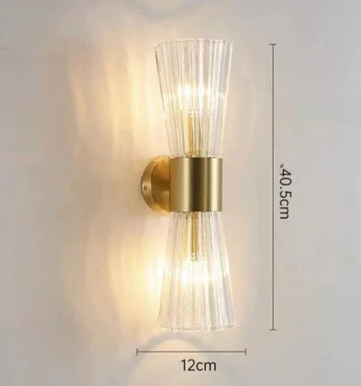 Wall-mounted light fixture with gold finish and clear glass shade on a white background