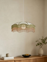 A white fabric umbrella pendant light with layered green and pink fringe hanging over a wooden cabinet.