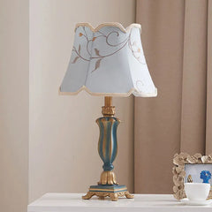 Ornate table lamp with a teal and gold resin base and a light blue fabric lampshade featuring a floral pattern, scalloped edges, and gold trim.