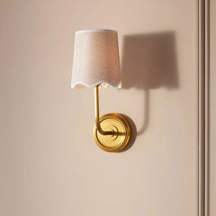Wall-mounted lamp with a white shade and gold base on a beige wall.