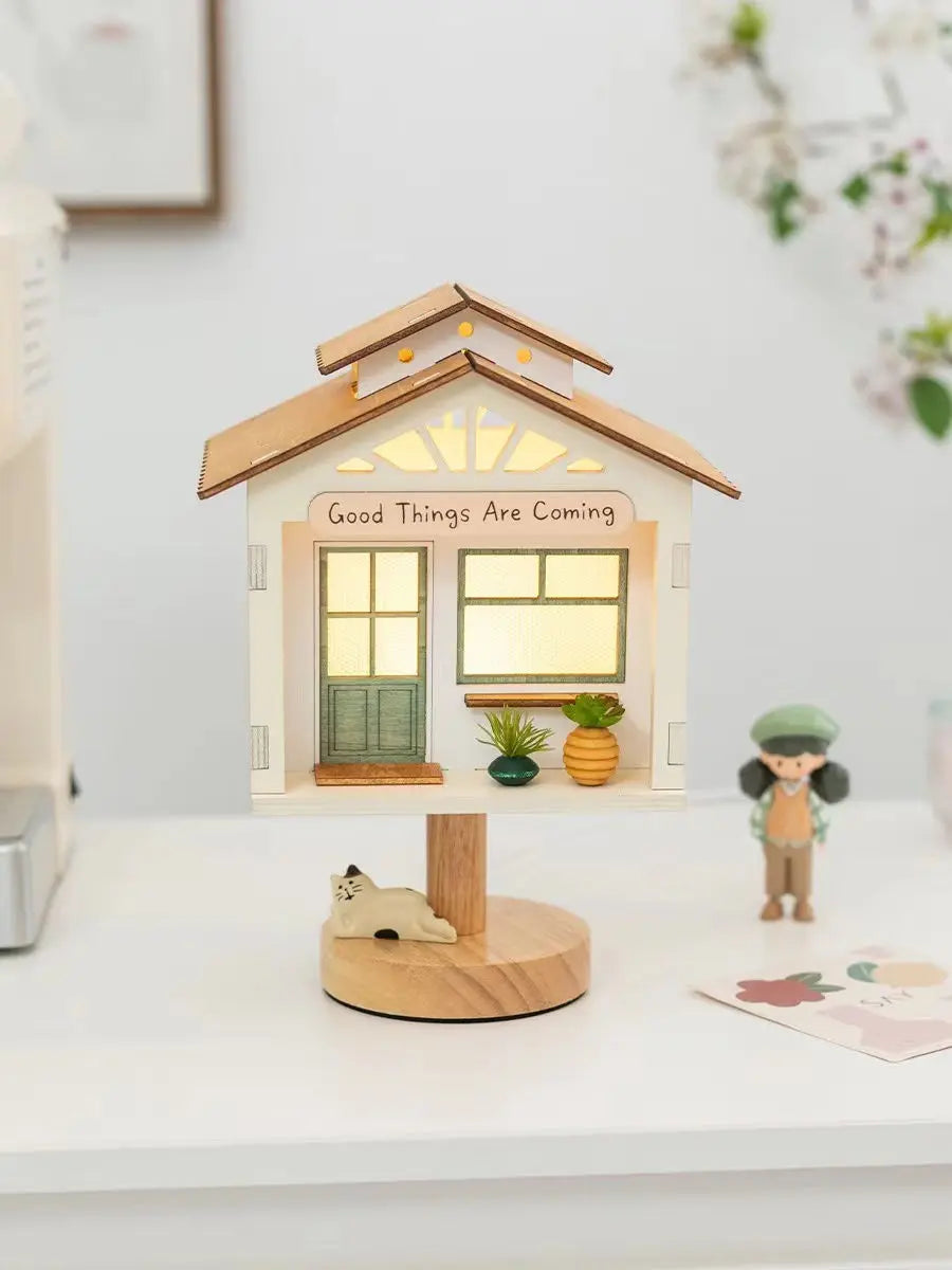 Close-up of the illuminated white tree house table lamp, showing the detail of the roof, windows, and base with small plants.