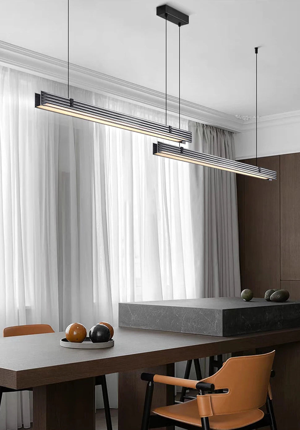 Modern pendant lights hanging above a dining table with chairs in a room with large windows.