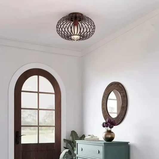 Brushed gold open cage semi-flush ceiling light mounted on a white ceiling in a hallway with a wooden arched door and a teal dresser.