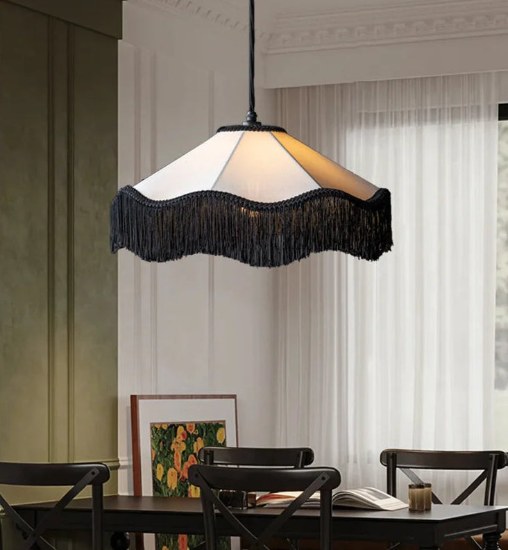 Fabric fringe pendant light with a white shade and black fringe, hanging in a dining room setting above a table.
