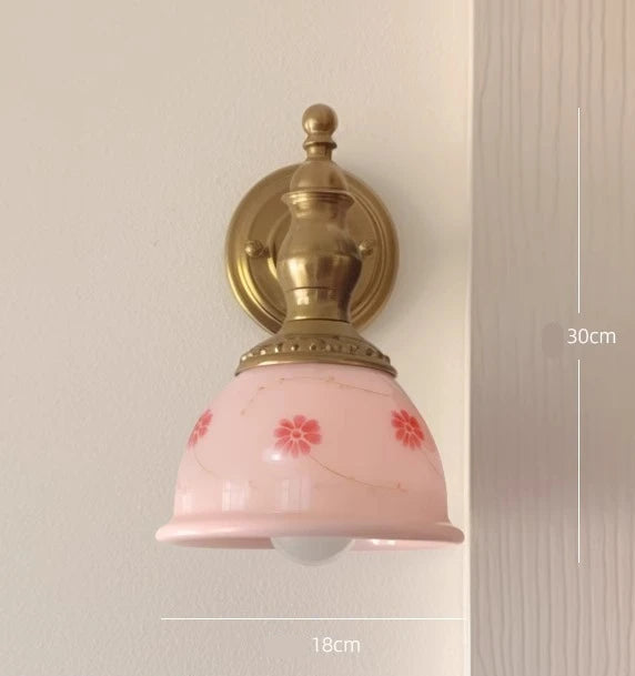 Wall-mounted light fixture with pink glass shade and gold fixture on a neutral background