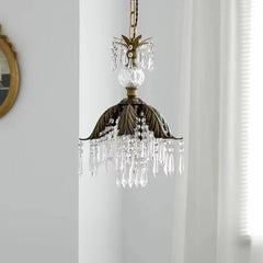Side view of a brass crystal chandelier with a leaf-shaped canopy, showcasing its detailed crystal droplets against a white wall.