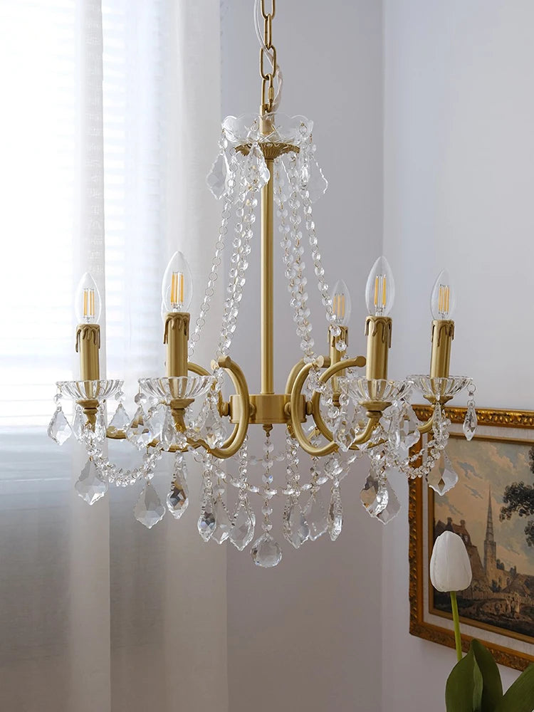 Gold chandelier with crystal accents hanging in a room with a painting and plant.