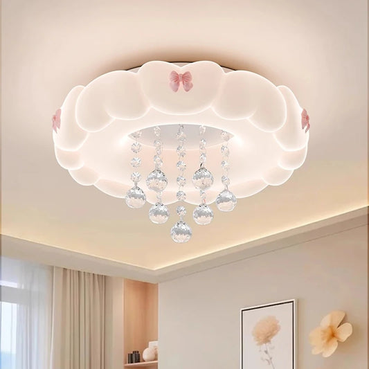 White cloud-shaped ceiling light with pink bows and crystal droplets hanging down, illuminated against a neutral ceiling.