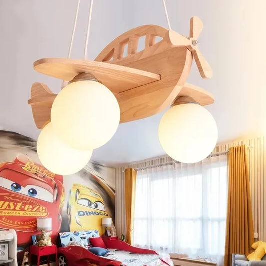 Close-up of a wooden airplane pendant light with milk white glass shades, suspended in front of a wall with Cars-themed wallpaper.