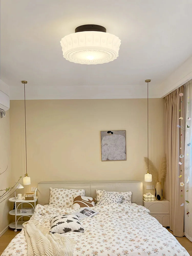Cream decorative glass pendant light with a black chain hanging in a bedroom with sheer curtains.