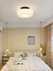 Cream decorative glass pendant light with a black chain hanging in a bedroom with sheer curtains.