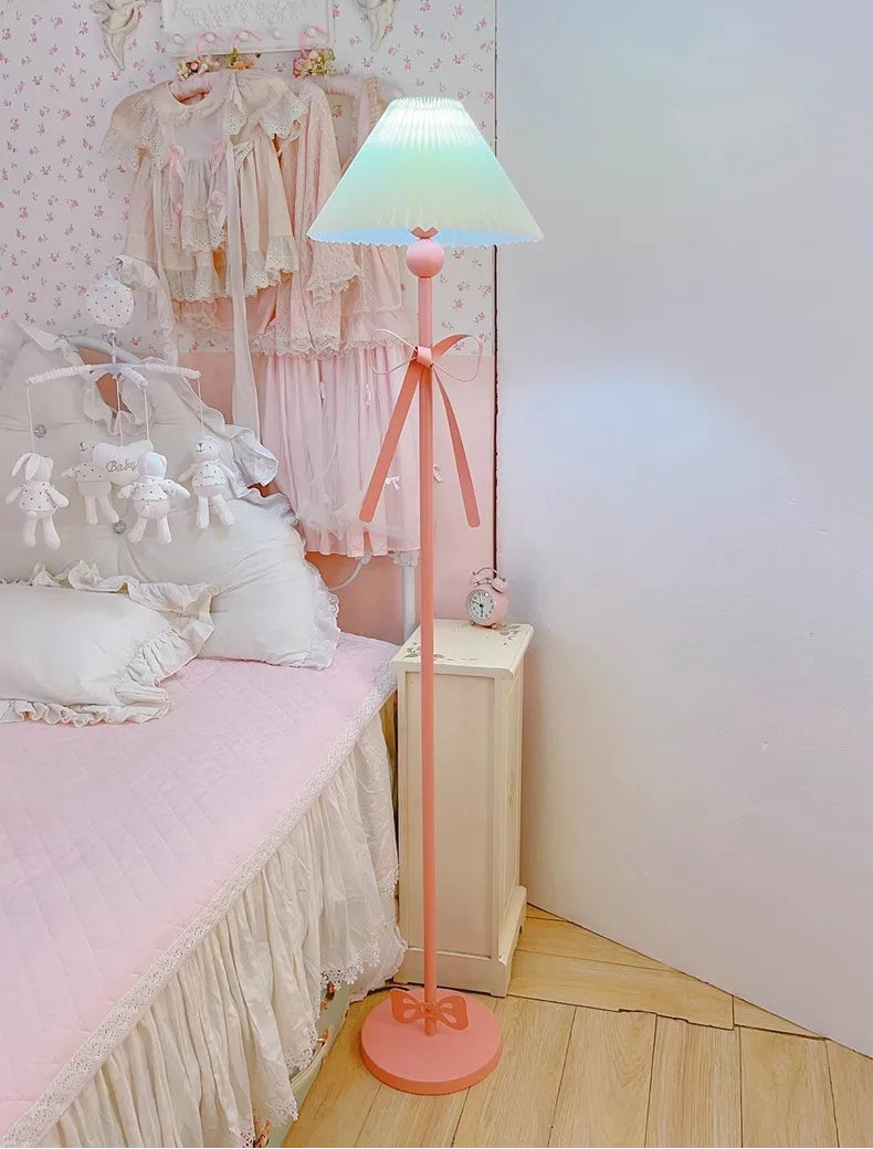 Pink floor lamp in a bedroom setting with a bed and nightstand.