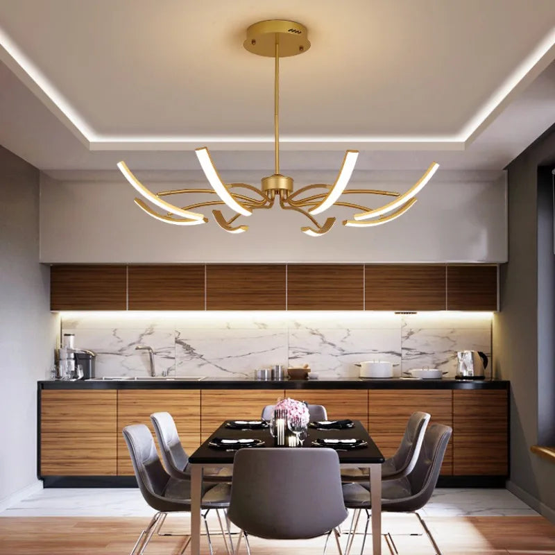 Gold chandelier with curved arms and LED lights above a dining table in a modern kitchen.