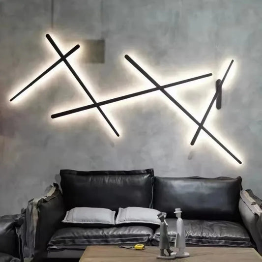 Black geometric line wall sconce mounted above a black leather couch, emitting a warm glow on a textured gray wall.