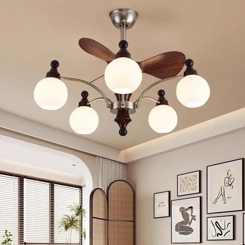 A metallic silver sputnik starburst ceiling fan chandelier with wooden blades and frosted glass globe lights, set against a neutral wall with artwork.