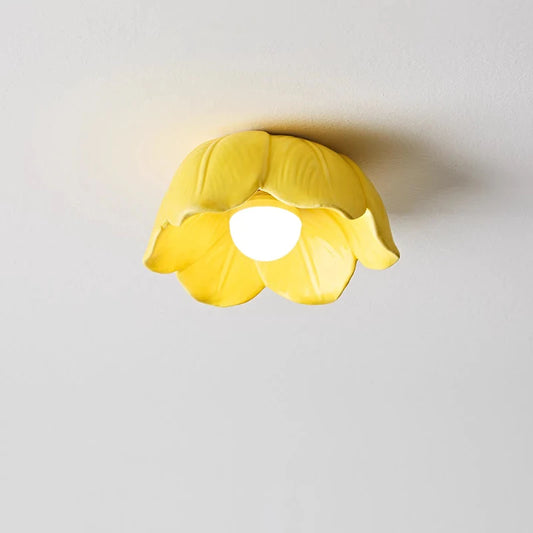 A yellow ceramic flower-shaped semi-flush ceiling light mounted on a white ceiling, lit by an internal LED bulb.