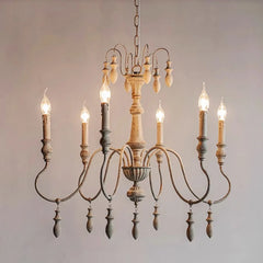Side view of a distressed white iron chandelier featuring multiple candle-style lights and decorative wooden drops.