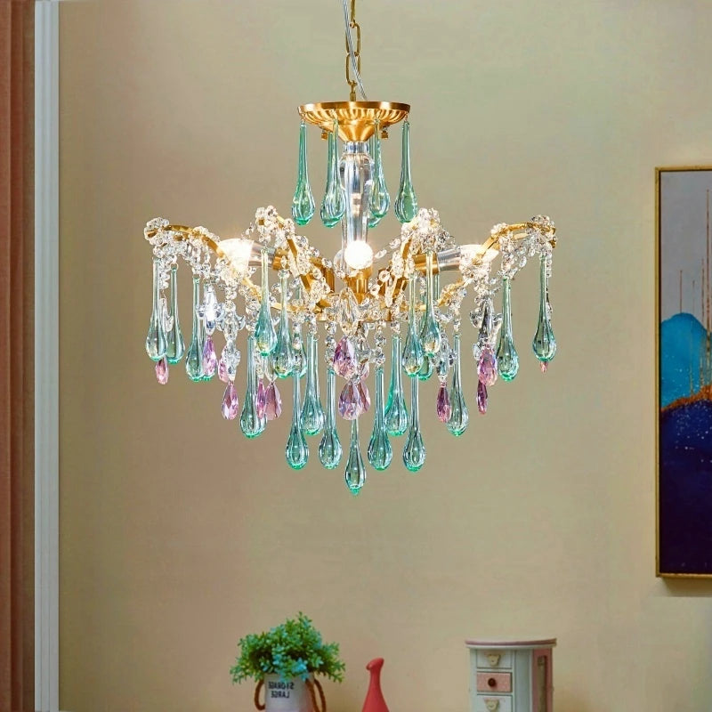 A gold cascading chandelier with pink and green teardrop crystals displayed above a piece of furniture.