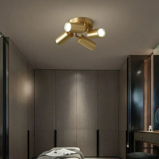 Brushed gold cylinder spotlights ceiling fixture above a bed.