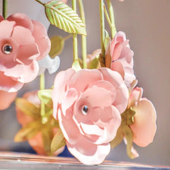 Detail shot of the pink floral petals and green leaves on the gold metal frame of a chandelier.