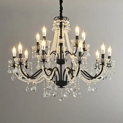 Black wrought iron candelabra chandelier with multiple arms adorned with clear crystal prisms and white pearl bead strands hanging against a gray backdrop.