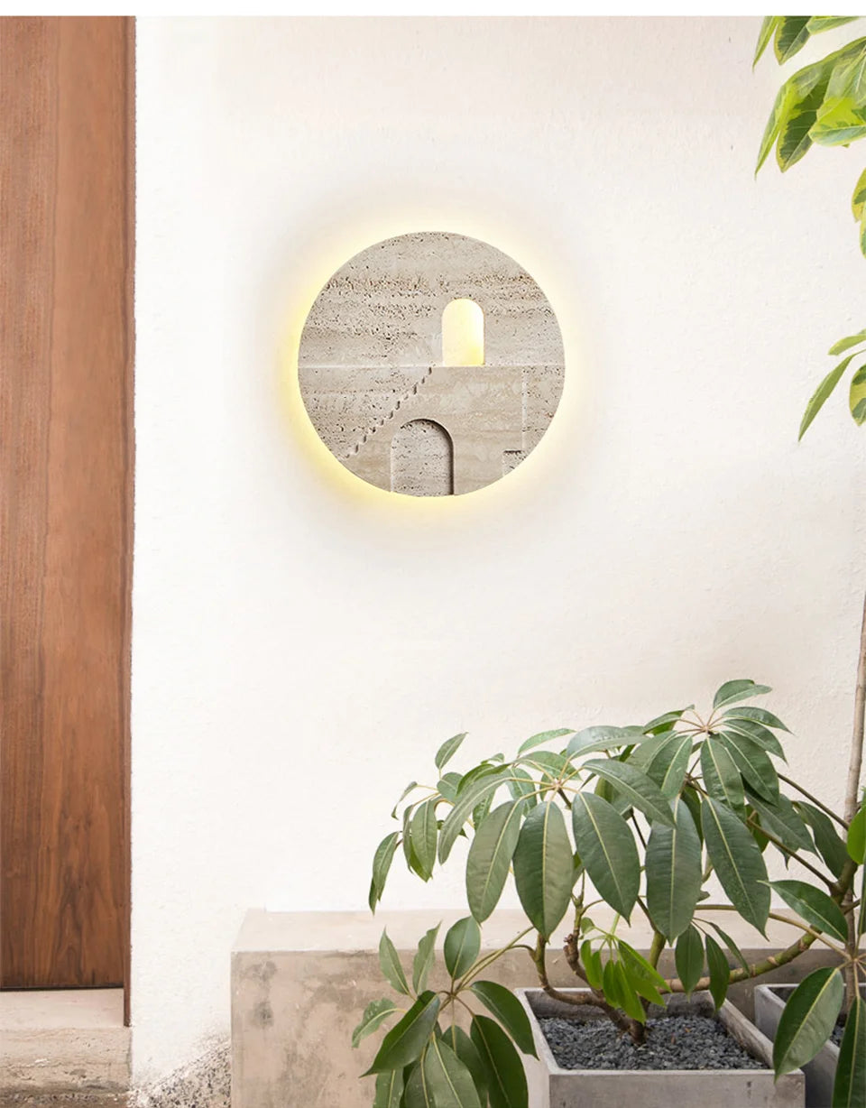 Round natural stone wall sconce with carved staircase and archway, mounted on a white wall next to a planter and wooden door.