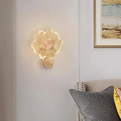 A gold flower glass wall sconce installed on a paneled wall in a living area, with a sofa and pillows visible.