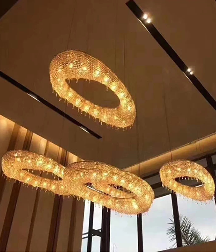Three circular chandeliers hanging from a ceiling with a window view in the background.