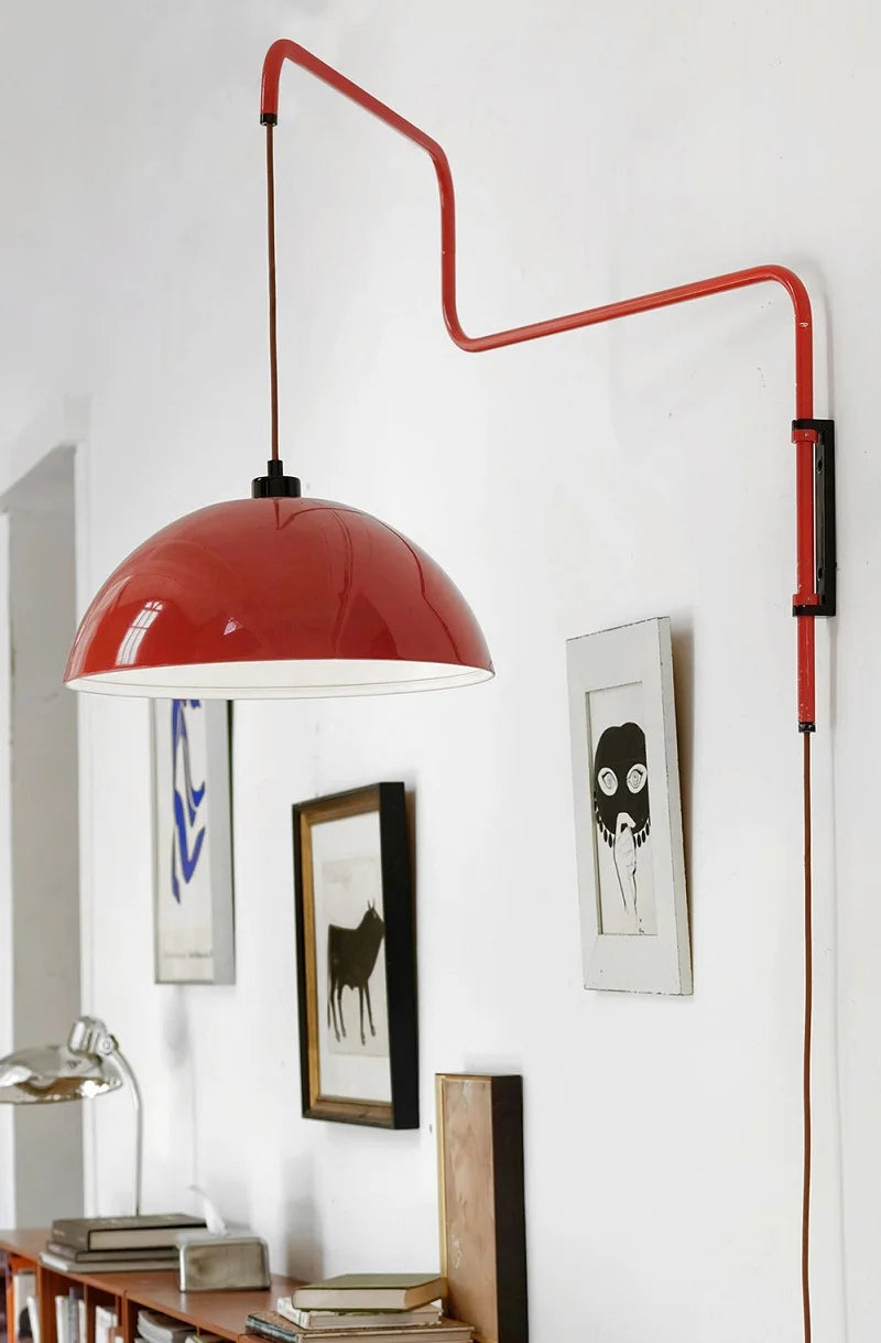 Red pendant lamp with a long arm in a room with framed pictures on the wall.