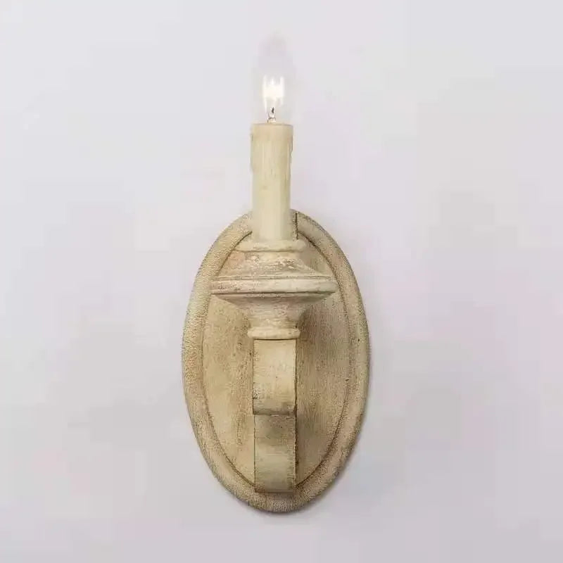A distressed wood candle wall sconce mounted on a white wall, with a single light illuminating.