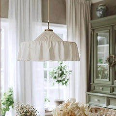 White pleated fabric pendant light with a metal accent at the top, viewed from below in a brightly lit room.