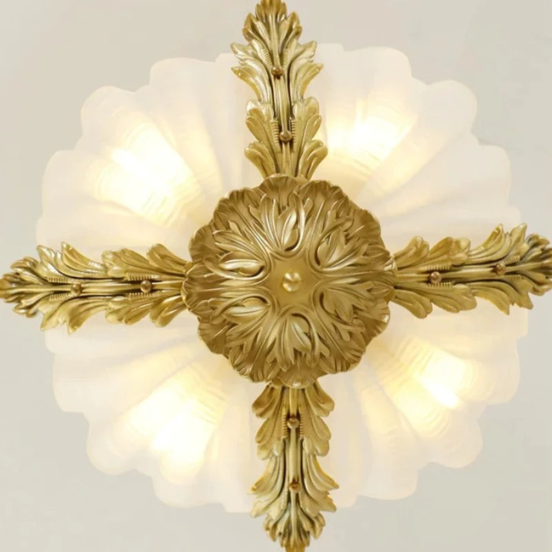 Overhead view of a pendant light, showing the four ornate gold leaf arms meeting at a central floral medallion, with the seashell glass diffuser emitting light.