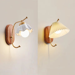 Two wall sconces side-by-side, one with a white ceramic flower shade and the other with a pleated cream fabric shade, both mounted on wooden bases with gold arms.