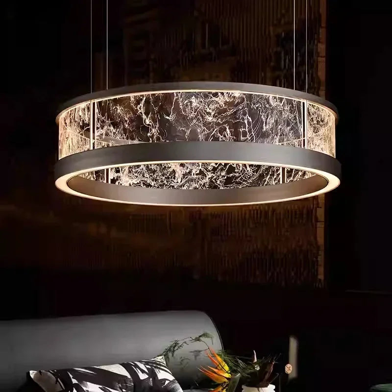 A large, dark-finished ring pendant light with a textured glass diffuser, hanging above a sofa and coffee table in a dimly lit room.